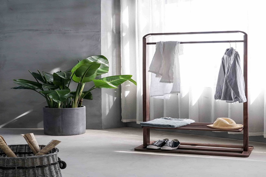 A wooden clothes rack in a room with a plant.
