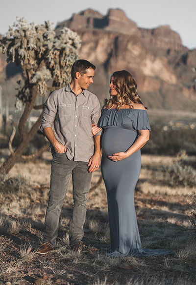 A pregnant couple standing in the desert with cactus in the background.