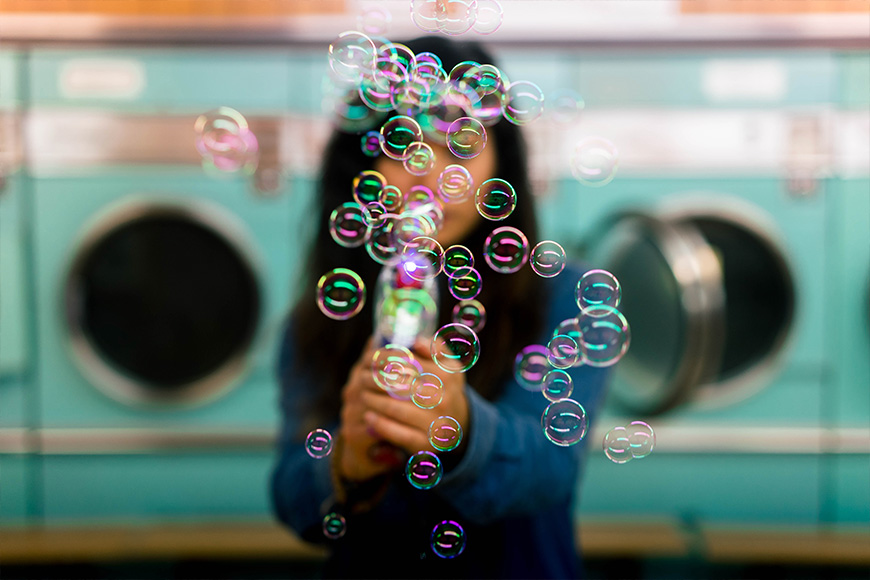 A woman blowing soap bubbles in a laundry room.