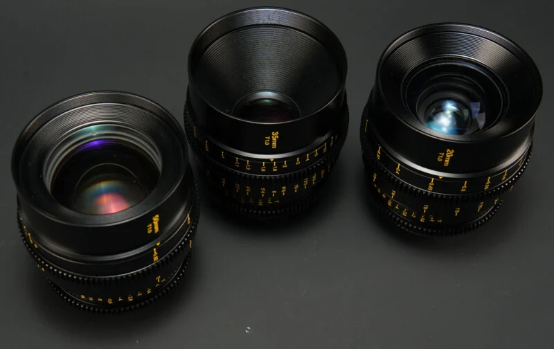 Three black camera lenses on a black surface.