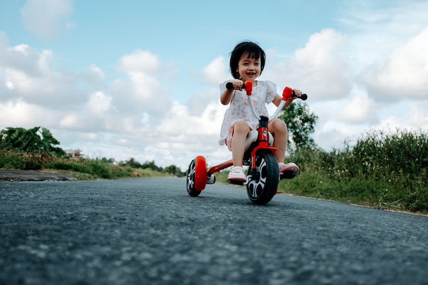 A little girl riding a red tricycle on a road.