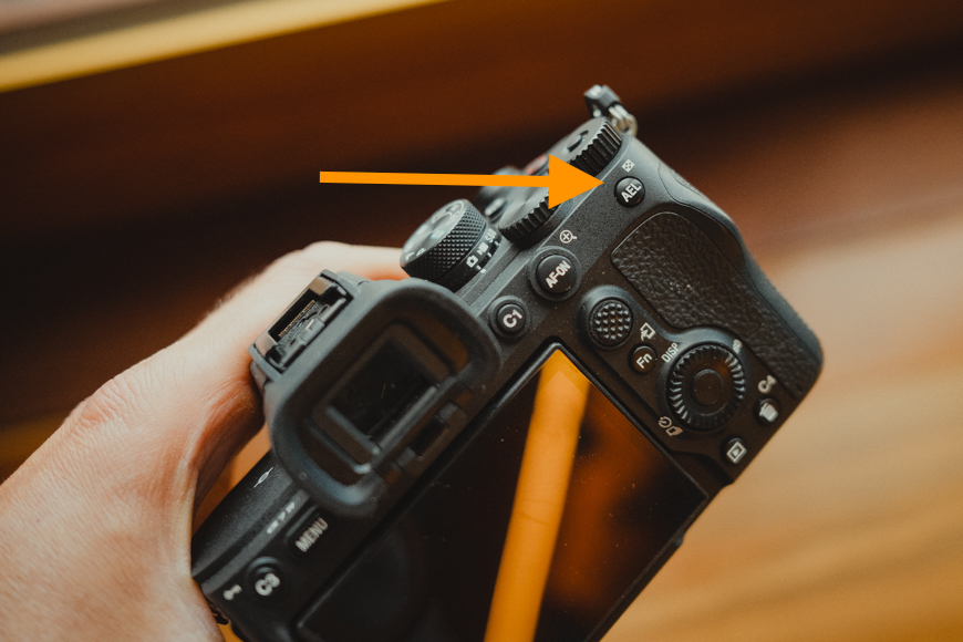 A person holding a camera with an orange arrow pointing at it.