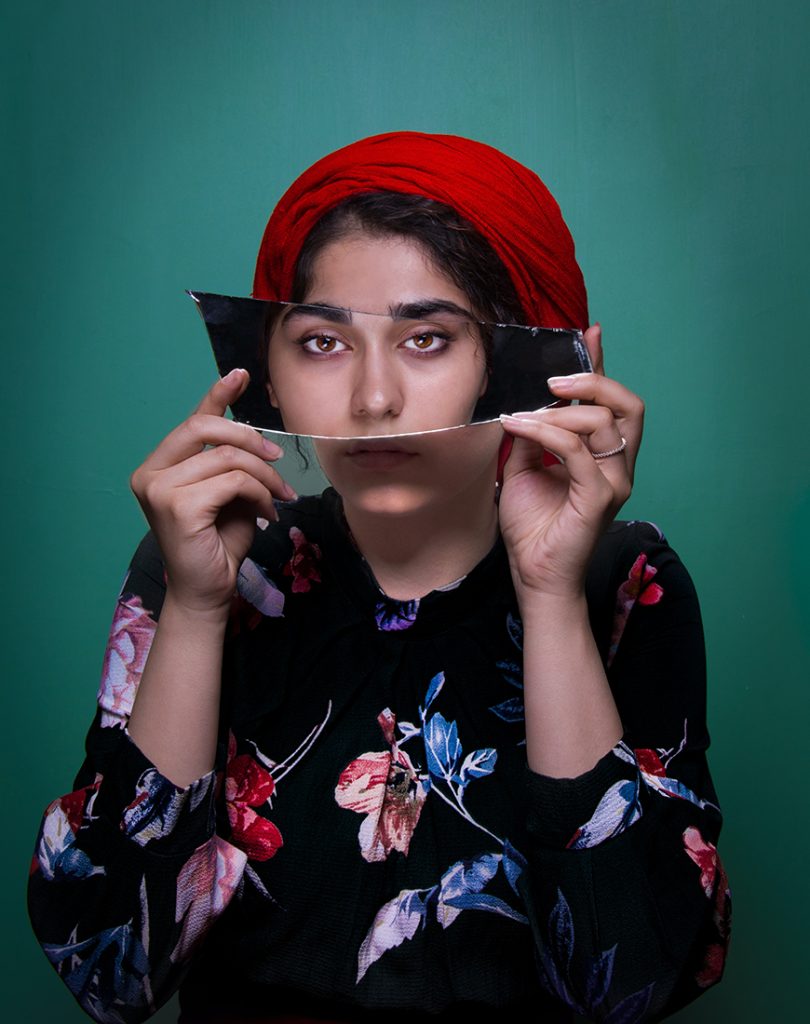 A woman is holding a mirror in front of her face.