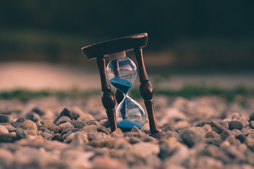 An hourglass sitting on the ground near a river.