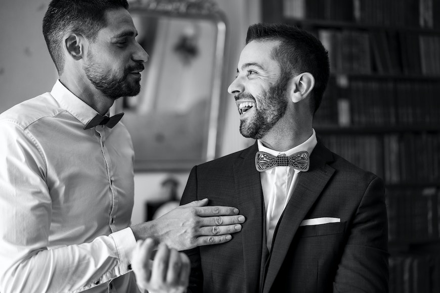 Two men in tuxedos laughing at each other.