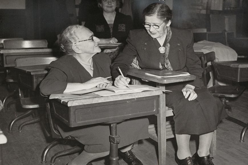 Two women sitting at desks in a classroom.