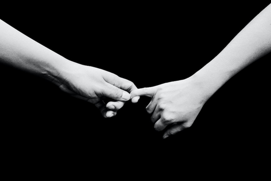 Two hands holding each other on a black background.
