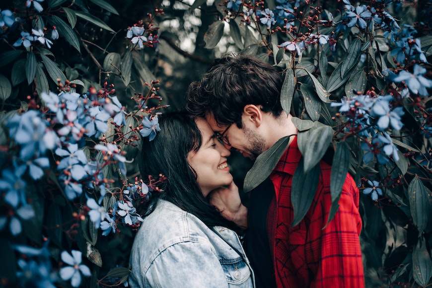 A couple embracing in front of blue flowers.