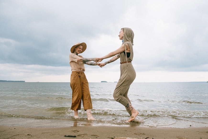 Two women standing on the beach holding hands.