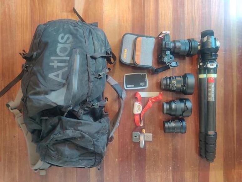 A backpack with camera equipment laid out on a wooden floor.