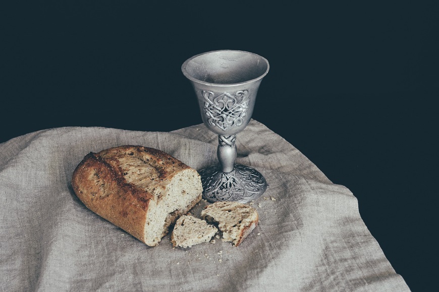 A silver goblet next to a piece of bread.