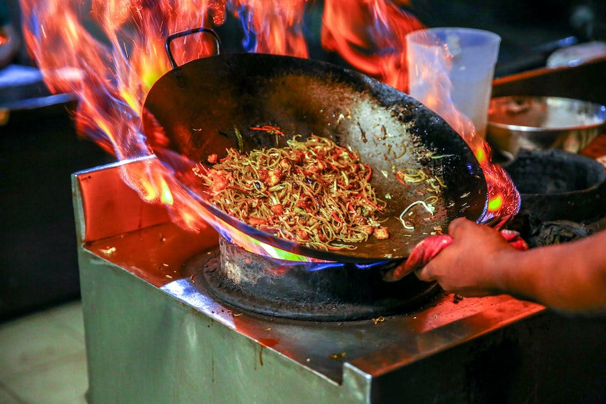 A person is cooking food in a wok on fire.