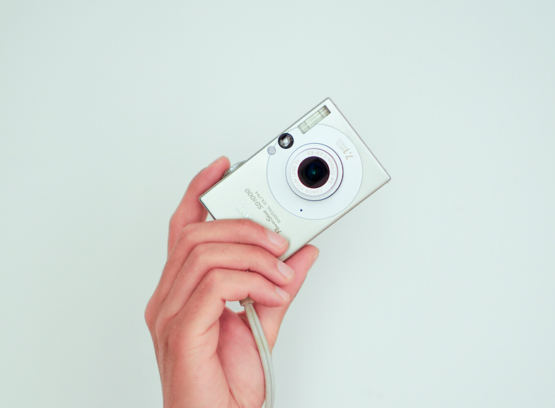 A woman's hand holding a camera on a white background.