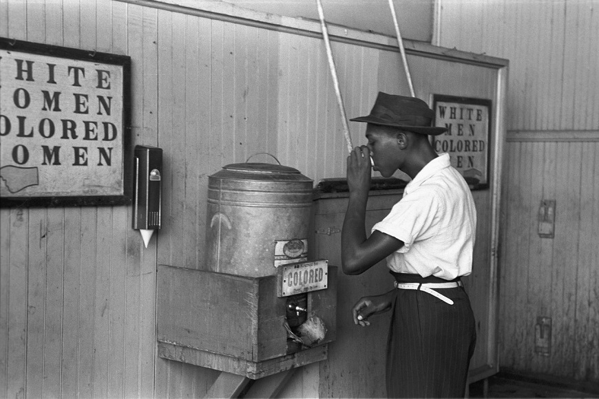A man in a hat is using a machine to wash his hands.