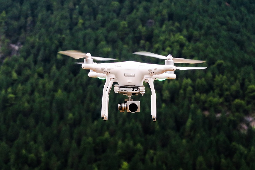 A white drone flying over a forest.