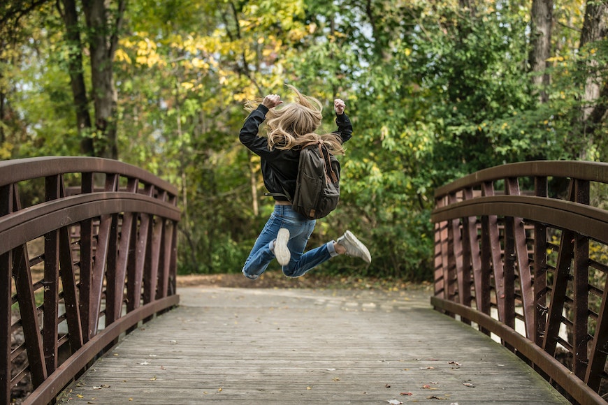 A young girl jumping over a bridge in the fall.