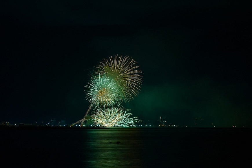 A green and white fireworks display over a body of water.