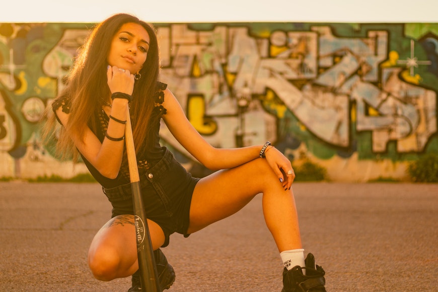 A girl posing with a baseball bat in front of graffiti.