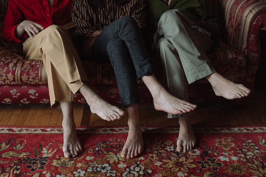 Three people sitting on a couch with their bare feet up.