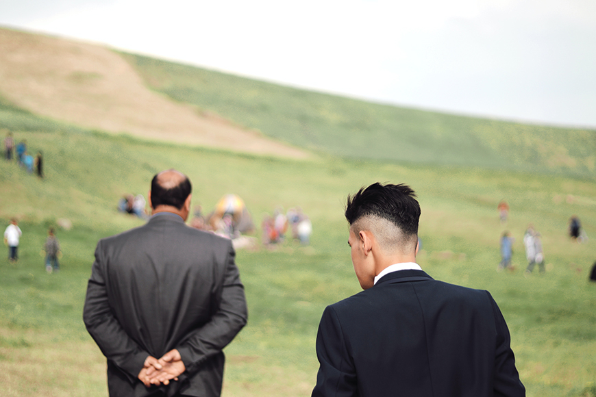 Two men in suits walking on a grassy field.