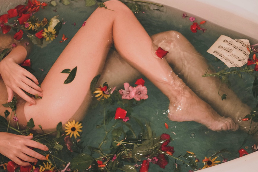 A woman is laying in a tub filled with flowers.