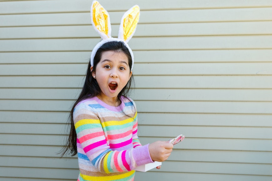 A young girl wearing bunny ears and holding an easter egg.