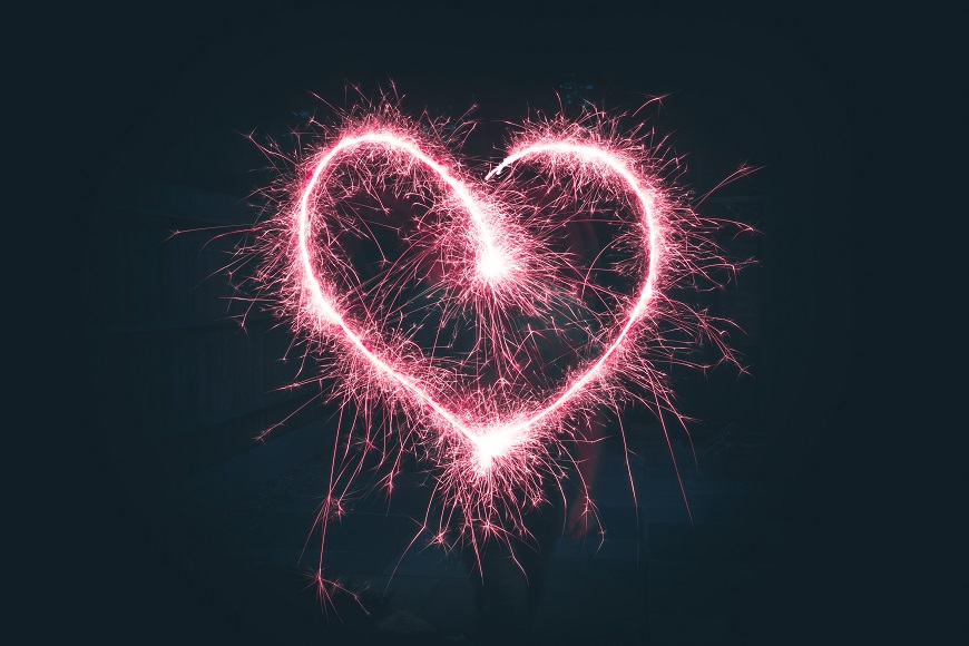 A person holding a sparkler in the shape of a heart.