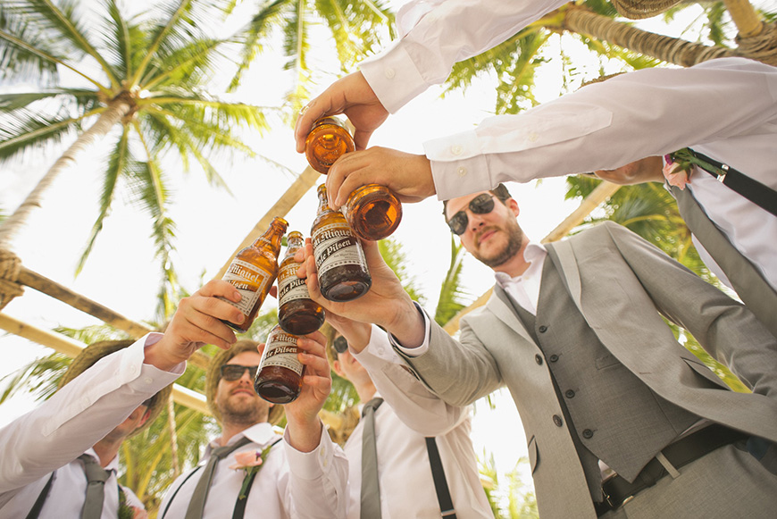 A group of groomsmen toasting with beer bottles.
