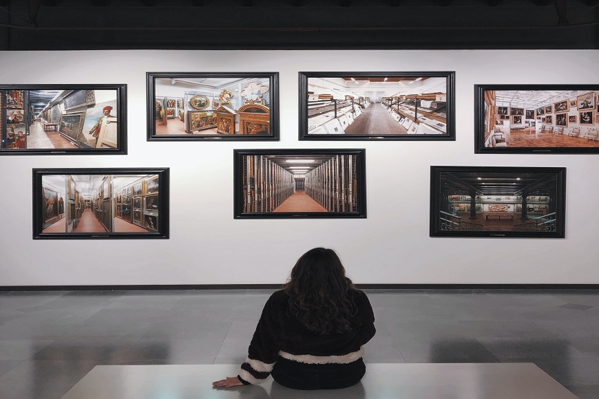 A woman sits on the floor in front of a display of photographs.