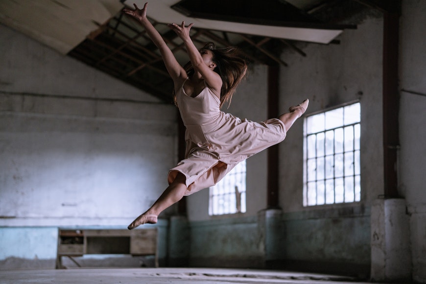 A woman in a pink dress is jumping in an abandoned building.