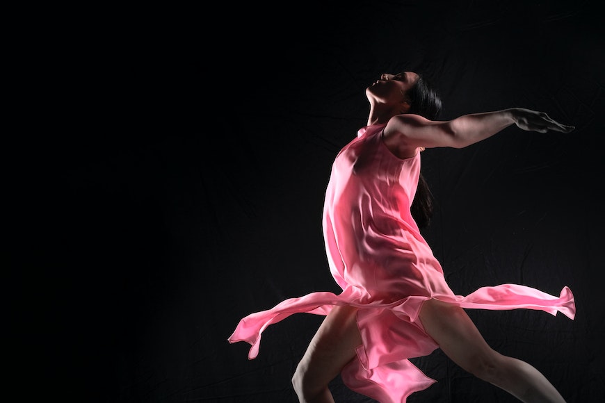 A woman in a pink dress is dancing on a black background.
