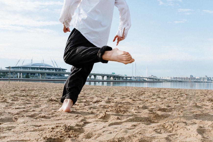 A man in a white shirt is kicking his feet on the beach.