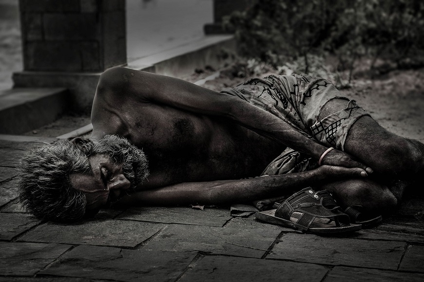 A homeless man laying on the ground in black and white.