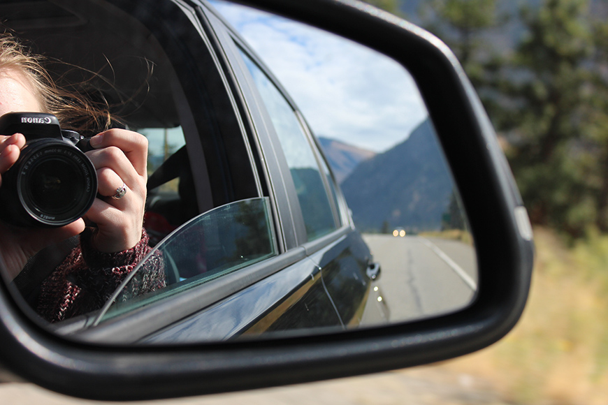 A woman is taking a picture in a car mirror.
