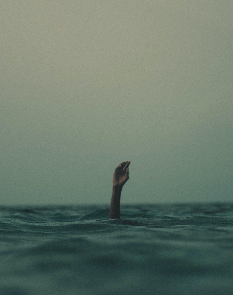 A hand reaching out of the water in the ocean.
