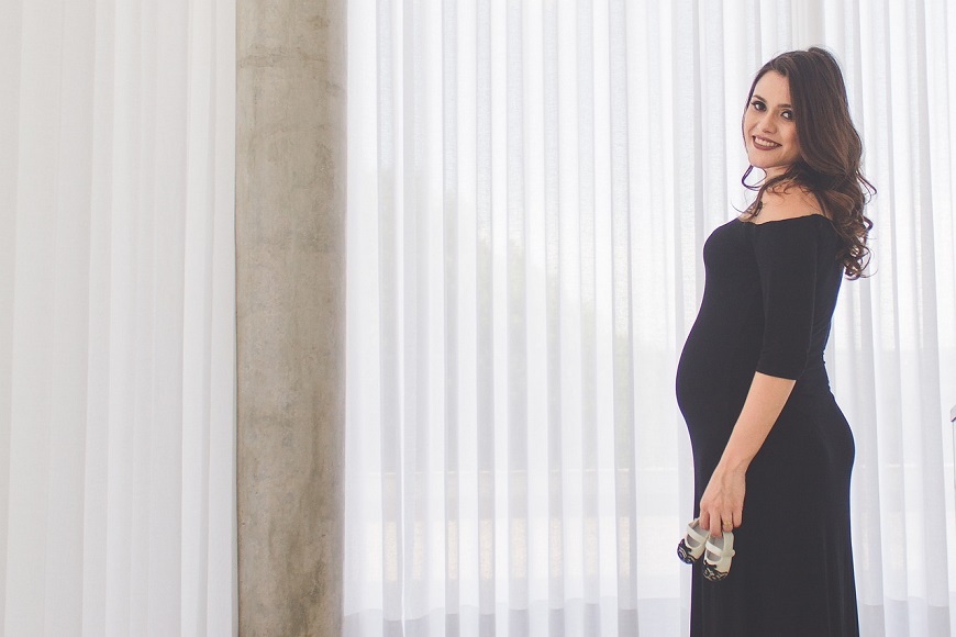 A pregnant woman in a black dress standing in front of a window.