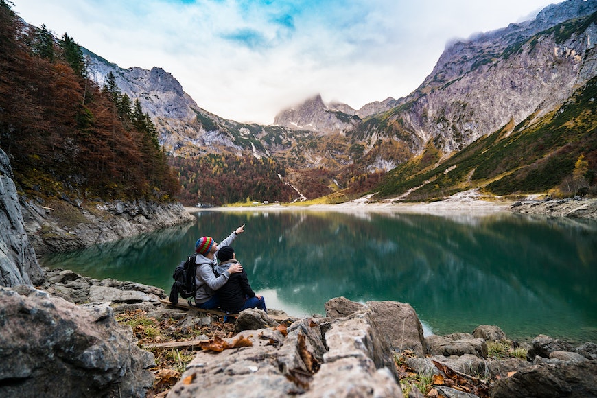 A couple sits on a rock next to a lake.