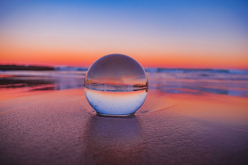 A glass ball sits on the beach at sunset.