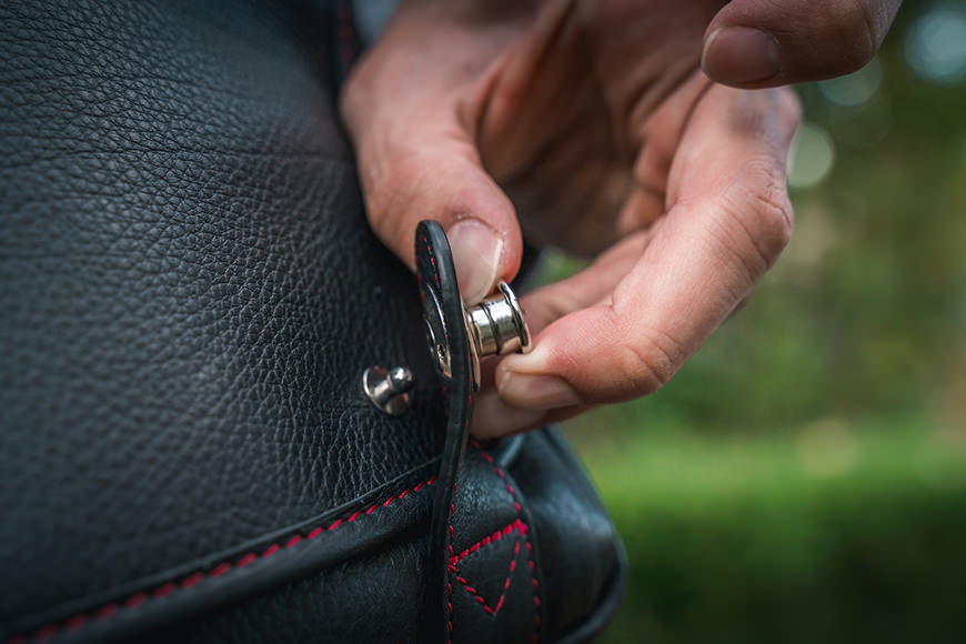 A person is opening a fastener on a black leather bag.