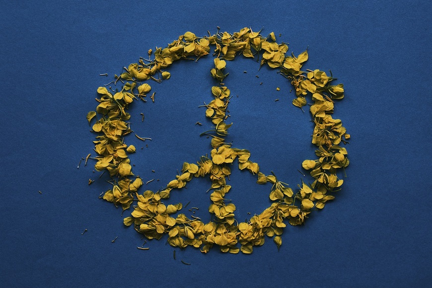 A peace sign made of yellow flowers on a blue background.