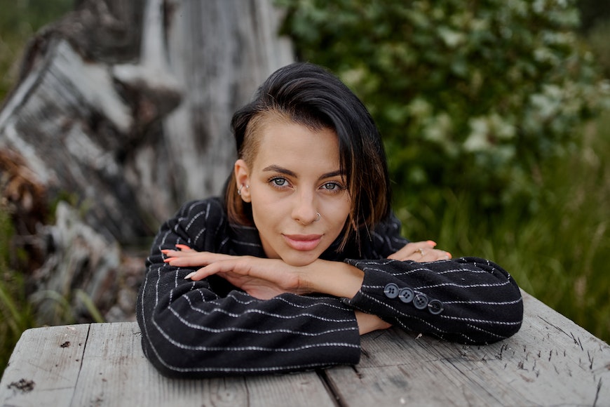 A woman with a shaved head posing on a wooden table.