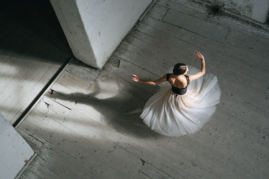 A ballerina in a white dress is dancing on a concrete floor.