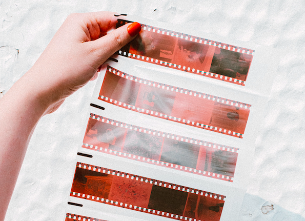 A person holding a film strip in front of a white wall.