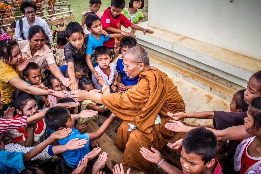 A buddhist monk greets a group of children.