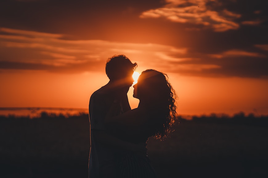 A silhouette of a couple kissing in front of a sunset.