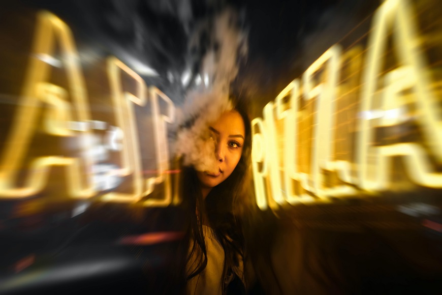 A blurry image of a woman smoking a cigarette in front of a neon sign.