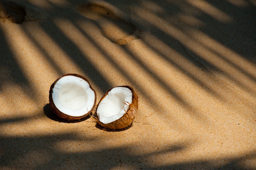 Two coconuts on the sand with shadows.