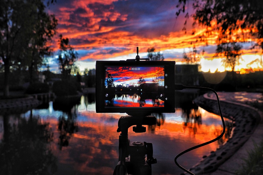 A photo of a sunset with a camera on a tripod in front of a pond.