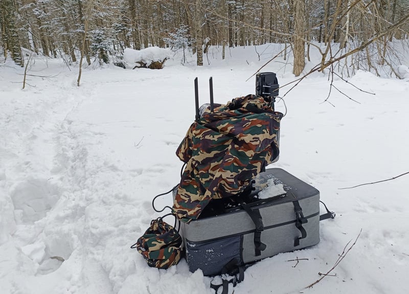 A camouflaged backpack sitting on top of snow in the woods.