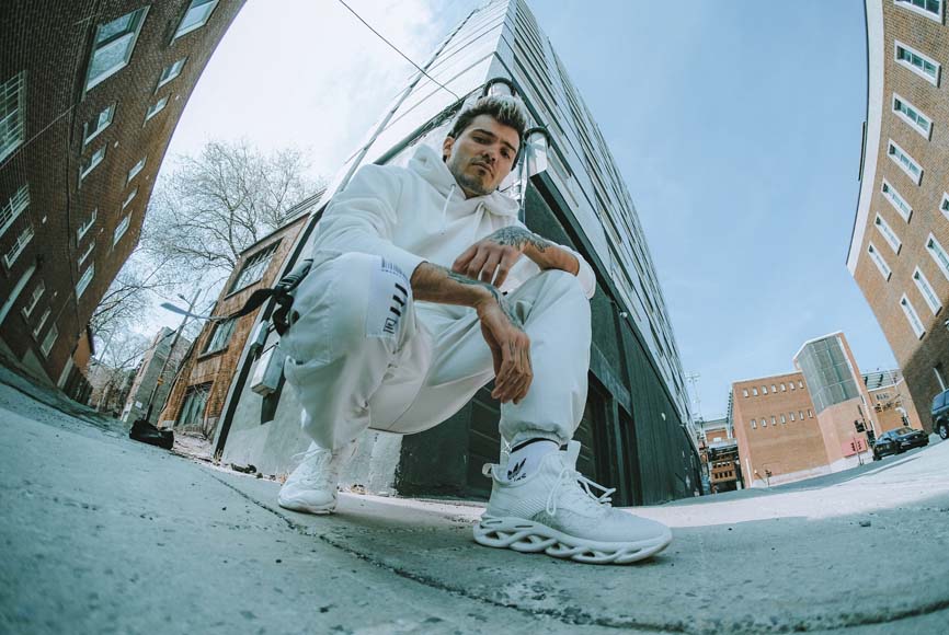 A man crouching in front of a building in white sneakers.